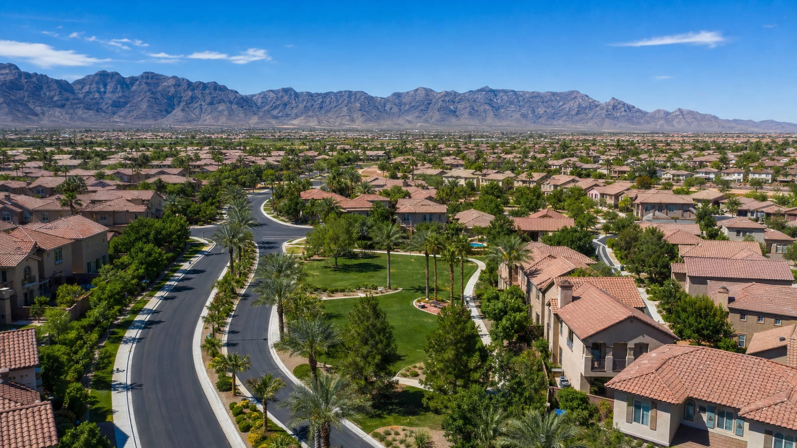 Aerial view of a Northwest Las Vegas master-planned neighborhood with a green community park, tile-roofed homes, and the desert mountain range beyond